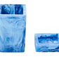 Two blue, marbled square resin containers from Nashi Home’s Denim Resin Bath Collection are displayed—one upright and tall, the other short and on its side—perfect additions to any modern bathroom.