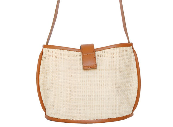 Handwoven beige raffia Bembien Paola Crossbody mini bag with a brown leather strap and closure flap against a white background.
