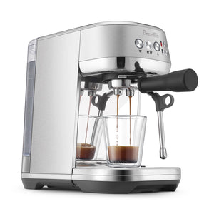 The Breville Bambino Plus Espresso Machine, made of stainless steel with a ThermoJet heating system, brews specialty coffee into two clear glass cups and features an automatic steam wand on the right side.