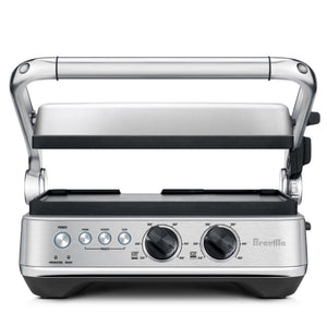 The Breville Sear & Press Grill is a stainless steel countertop grill with adjustable top lid, front control dials, and buttons, serving as a versatile panini press for delicious sandwiches and grilled foods.