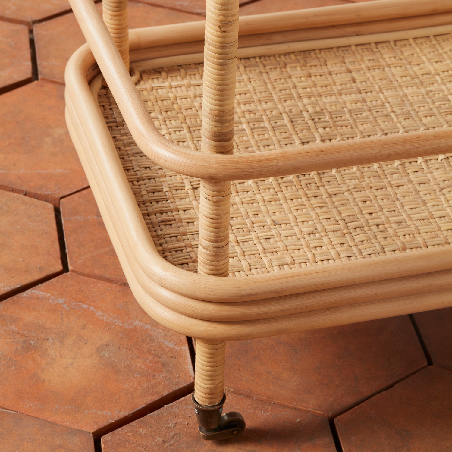 Close-up of the Selamat Flore Bistro Bar Cart, featuring Manau rattan and wood with rounded edges and caster wheels, evoking French café style, set on a hexagonal terracotta tile floor.