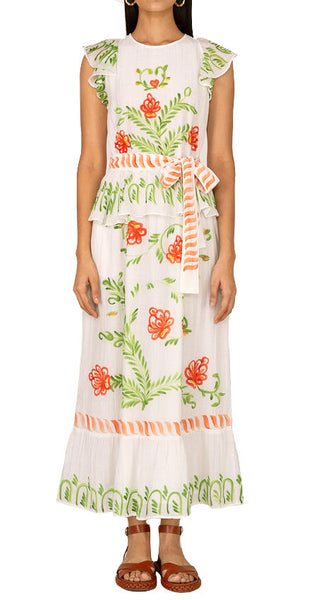 Woman in a white and floral patterned Banjanan Basha dress with a ruffled neckline and hem, standing against a neutral background.