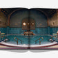 An open book, titled "Budapest Gem" by Assouline, reveals an image of an ornate indoor swimming pool reminiscent of Budapest's grandeur, adorned with mosaic tiles, columns, and decorative walls.