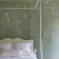 The Garbo King Bed by Bunny Williams features cylindrical posts and spherical finials, shown here in white lucite against a distressed green textured wall, topped with white bedding and a decorative pillow.