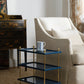 The Bunny Williams Tiered Drinks Table, finished in blue and gold lacquer with brass finials and a striped mug on top, sits beside a cream-colored armchair in the living room—an instant conversation starter.