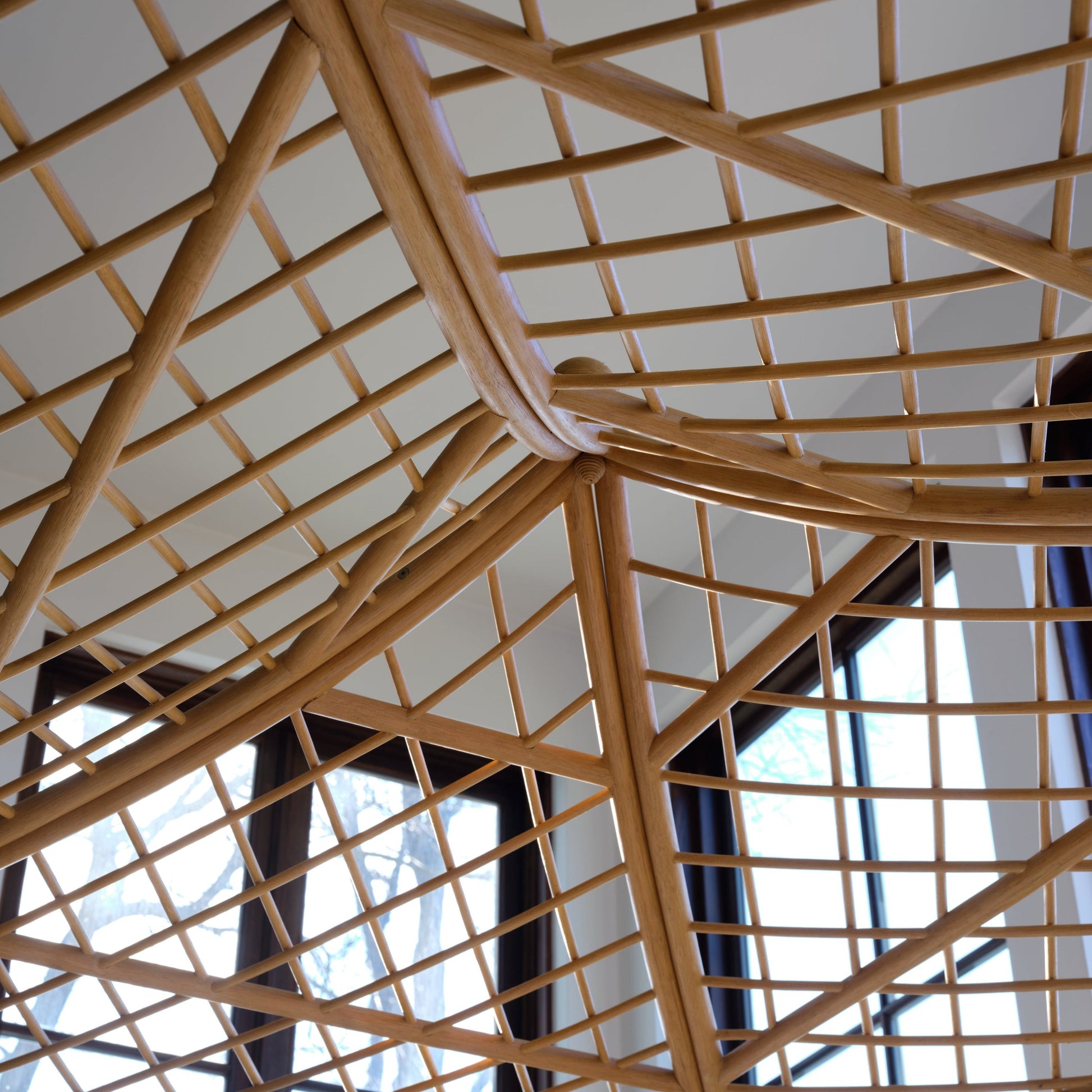 The Bunny Williams Rattan Trellis Canopy Bed, with its striking lattice design of intersecting beams, stands out against large windows and a white ceiling.