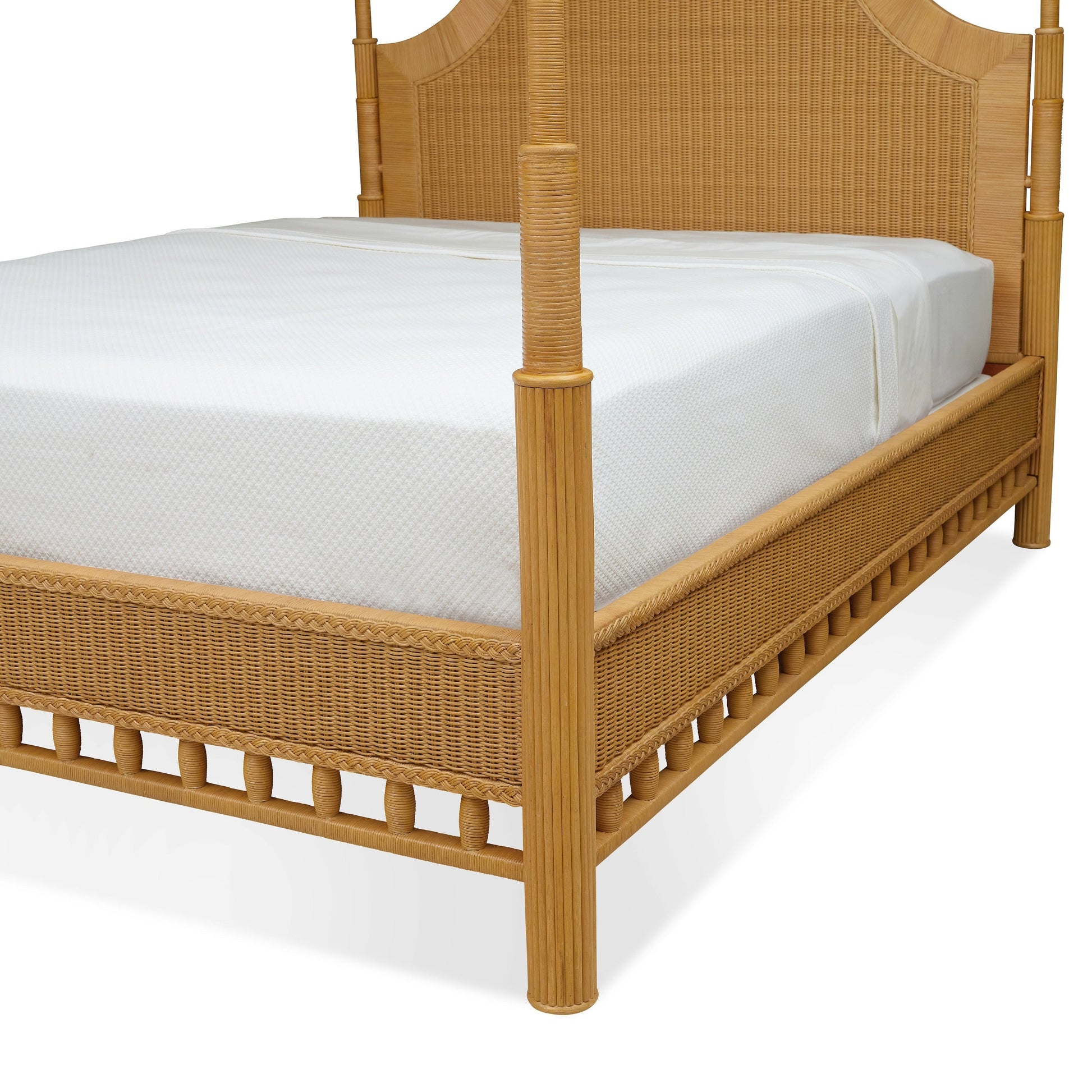 A close-up of the Bunny Williams Rattan Trellis Canopy Bed showcases its wooden frame with woven wicker and white mattress, highlighting the subtle lattice design.