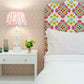 A playful bedroom features the EJ Schrader Rosa Spring Twin XL Bed with white bedding and a floral headboard, paired with a bedside table holding a lamp, glass vases, and flowers against a pink wallpapered wall.