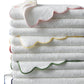The Matouk Cairo Scallop Bath Collection features luxury long-staple cotton towels with scalloped edges, each trimmed in a unique pastel color and shown neatly folded against a plain background.