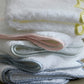 A stack of Jasper Bath Collection towels by Matouk, featuring white fabric with scalloped edges and colored trim in yellow, pink, light blue, and dark blue, is beautifully arranged on a wooden surface.