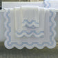 Matouk’s Mirasol Bath Collection towels, featuring scalloped blue-trimmed edges, are draped over a white bathtub, with another Cairo cotton terry towel visible on the edge in the background.