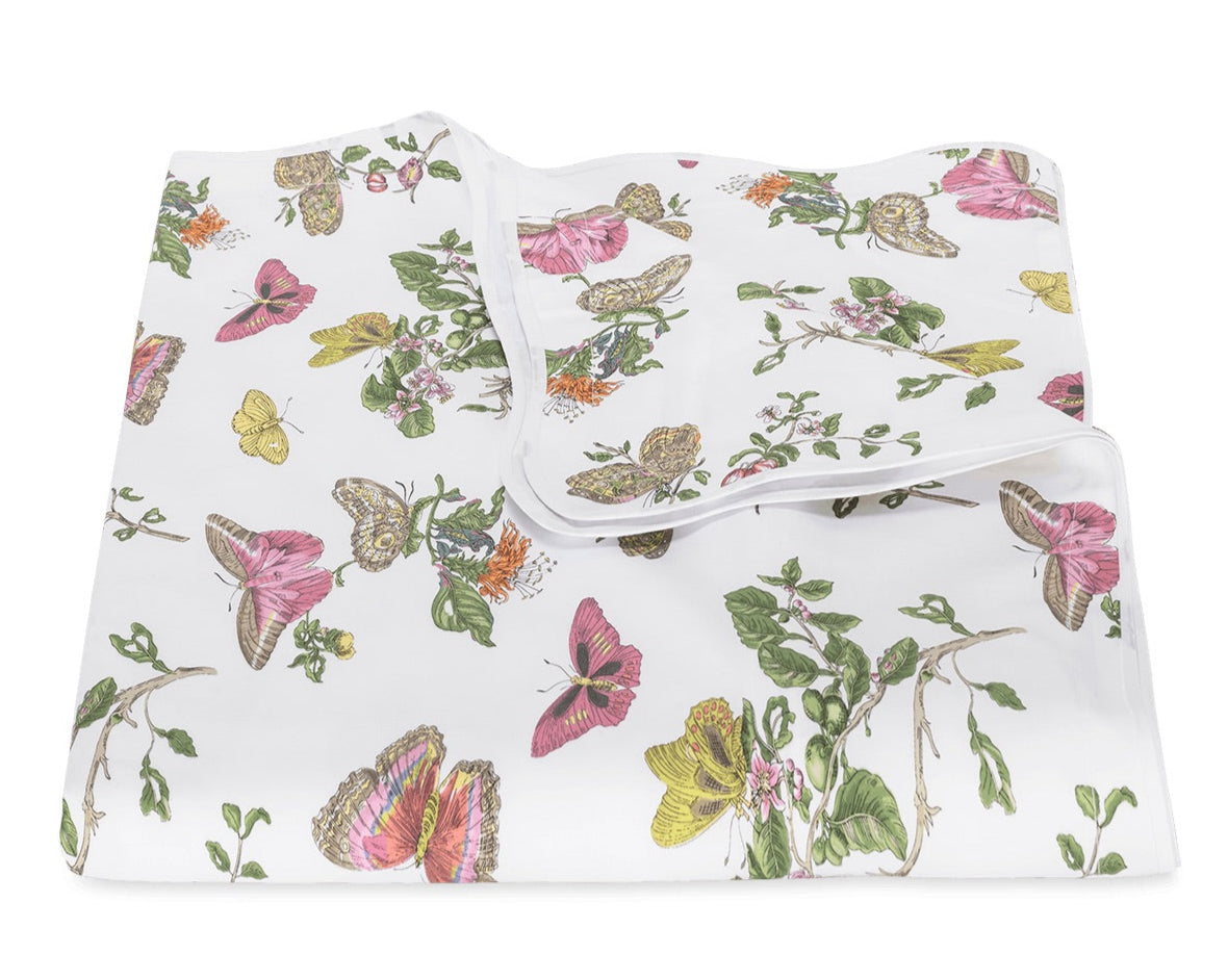 The Baudin Butterfly Pink Bedding Collection by Matouk is a folded white blanket adorned with vibrant butterfly and botanical floral prints in pink, yellow, green, and brown.