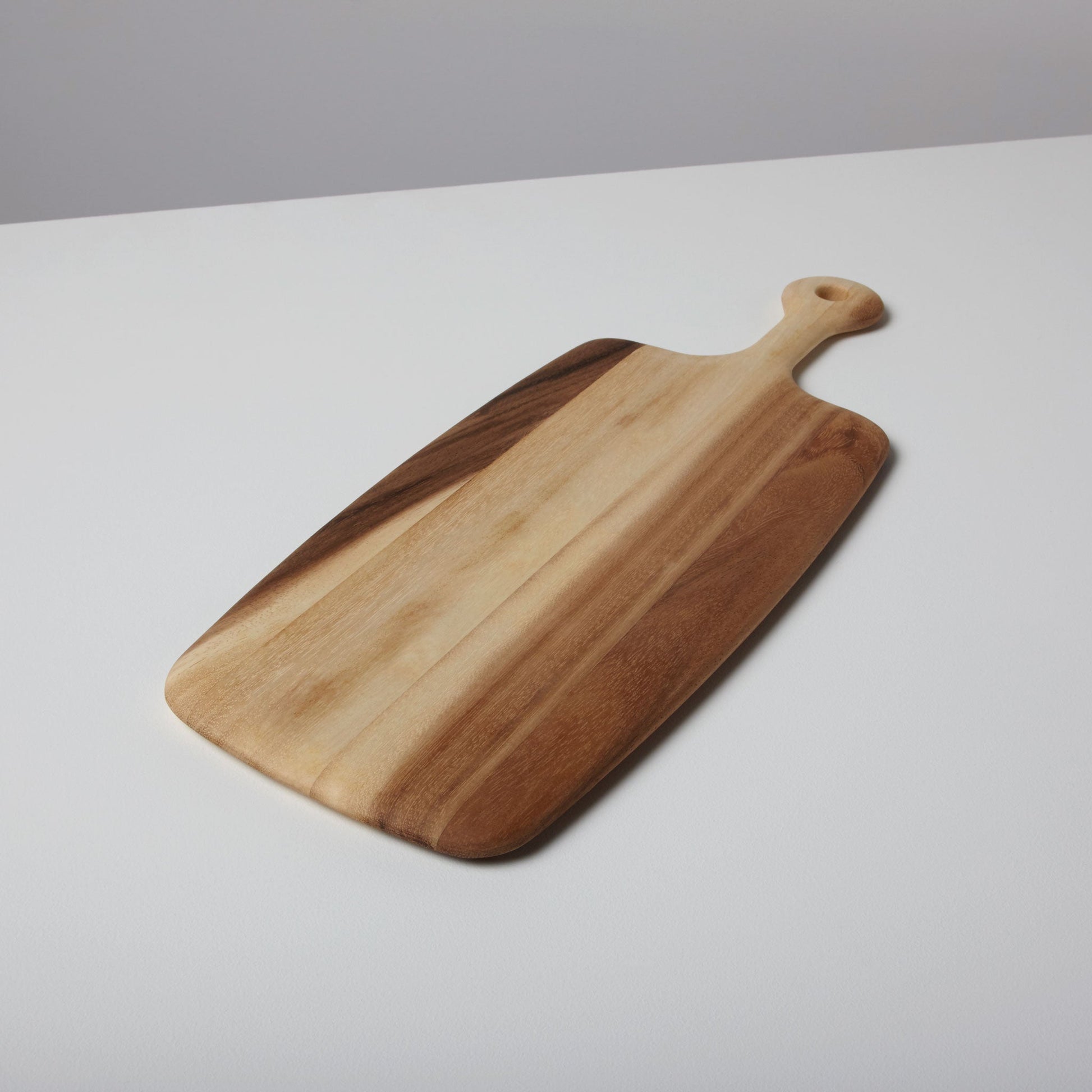 The Be Home Acacia Wood Rectangular Board with Handle Collection features a board with a handle and hole, showcased on a white surface.