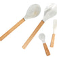 The Be Home Shell and Bamboo Serving Collection features four utensils—salad fork, spoon, spatula, and small spoon—with wooden handles and white heads, highlighting ethical craftsmanship against a clean white background.