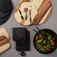 The Be Home Acacia Wood Round Board Collection, paired with cheese knives and a black bowl of fresh salad with greens and tomatoes, is displayed on a gray surface.