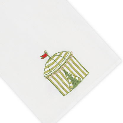 Haute Home’s Beach Cabana Bath Collection linen napkin features a white Italian linen fabric embroidered with a green and white striped cabana topped by a red flag.