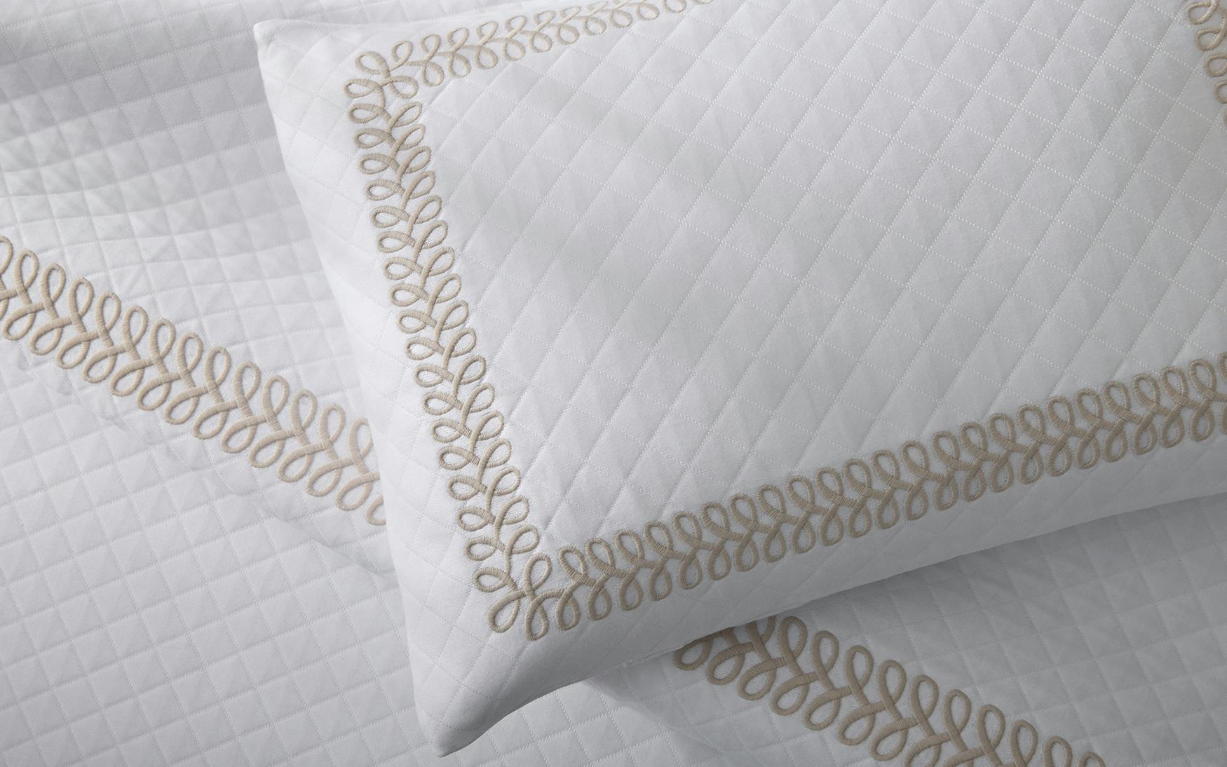 Matouk Astor Braid Matelassé Bedding Collection in Dune, featuring a white quilted pillow and sheet with beige braid embroidery loop border, shown from above.