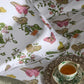 A bed dressed in Matouk's Baudin Butterfly Pink Bedding Collection—white Egyptian Cotton sheets and pillowcases with a vibrant butterfly and botanical design—sits beside a tray with a cup of tea.