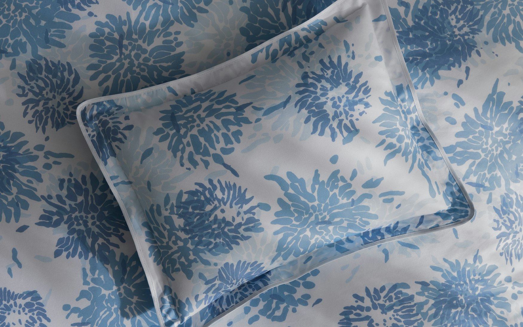 The Matouk Tillett x Matouk Chrysanthemum Bedding Collection in Blue features a pillow and bedsheet with a blue floral motif on a white background.