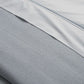 Close-up of the Matouk Costa Mesa Blanket Collection in light gray, highlighting its soft knitted texture and a smooth contrasting sheet, with visible seams and folds for added detail.
