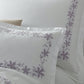 The Callista Bedding Collection by Matouk is elegantly displayed on a bed, featuring white pillowcases and sheets crafted from sumptuous Giza Egyptian cotton with light purple decorative embroidery—perfect for those who appreciate luxury bedding.