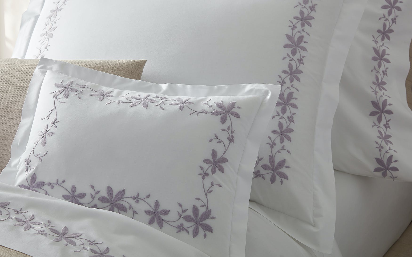 The Callista Bedding Collection by Matouk is elegantly displayed on a bed, featuring white pillowcases and sheets crafted from sumptuous Giza Egyptian cotton with light purple decorative embroidery—perfect for those who appreciate luxury bedding.