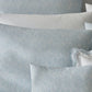 A close-up view of neatly arranged pillows and pillowcases from the Duma Diamond Bedding Collection by Matouk, showcasing light blue and white patterns in luxurious Egyptian cotton percale with both solid and decorative trim designs, accented by subtle geometric motifs.