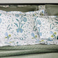 A bed featuring the Schumacher Khilana Bedding Collection in Blue by Matouk, with green quilted bedding and floral-patterned pillowcases and sheets in blue, green, and yellow hand-block textiles.