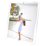A woman in a white dress lifts a child by the water’s edge, trees behind them—a moment as timeless as cherished photos showcased in Tara Wilson Designs’ Clear Beveled Frame Collection.