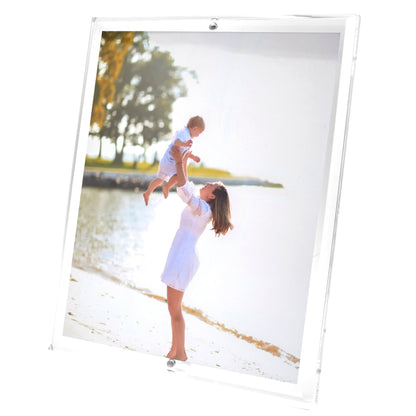 A woman in a white dress lifts a child by the water’s edge, trees behind them—a moment as timeless as cherished photos showcased in Tara Wilson Designs’ Clear Beveled Frame Collection.