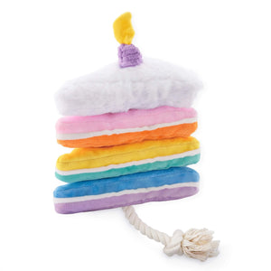 The Foggy Dog Birthday Cake Interactive Snuffle Dog Toy is shaped like a vibrant rainbow layer cake complete with a yellow candle on top and a sturdy rope tail at the bottom, making it perfect for playful pups who enjoy both snuggling and tug-of-war games.