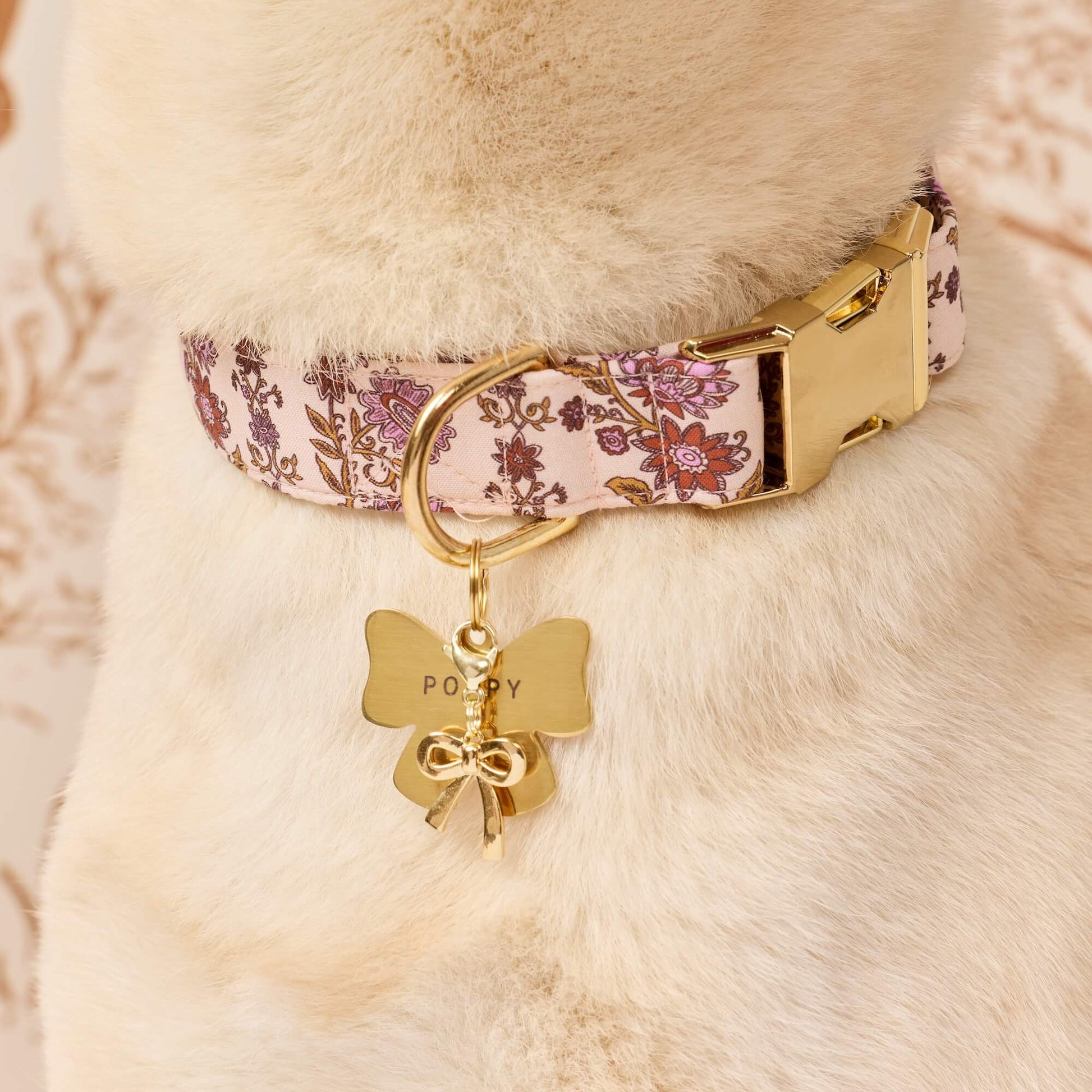 A dog wears The Foggy Dog Blockprint Floral Dog Collar paired with a gold butterfly-shaped tag engraved with “POPPY.”.