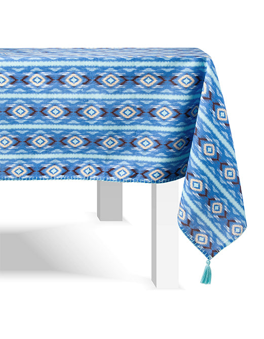 The Figue Diamond Ikat Clearwater Table Linen Collection features a blue and white geometric tablecloth with tasseled corners, ideal for adding vibrant style to any white rectangular table and pairing with your favorite napkin set.