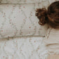 A person with brown hair lies on a bed adorned with the Botanical Berries Bedding Collection by Gooselings, featuring a white pillow and sheet patterned with delicate strawberries and vines. The cozy scene evokes bedtime dreams, while the charming bedding recalls classic children’s collections. The person’s face is not visible.