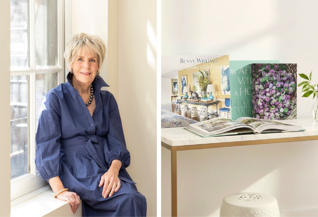 An older woman in a blue dress sits by a window next to a table with design books and an open book, capturing the vibe of the Bunny Williams Book Signing by HIVE Home, Gift and Garden.