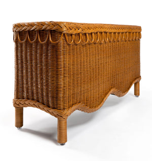 The Bunny Bench by Sharland England is a rectangular natural rattan bench with curved decorative edges and four short legs, shown against a white background.