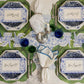 A table set for four with blue and white plates, green glasses, silver-ringed white napkins, Hester & Cook Die Cut Cabbage Placemats, place cards that say “Bon Appetit!”, all arranged on a floral table runner.