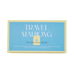 A rectangular box labeled "Travel Mahjong Set" by The Mahjong House features a blue background with yellow borders and white text, and contains lightweight tiles for the perfect portable mahjong set.