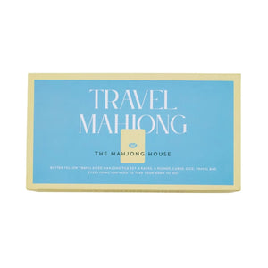 A rectangular box labeled "Travel Mahjong Set" by The Mahjong House features a blue background with yellow borders and white text, and contains lightweight tiles for the perfect portable mahjong set.