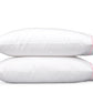 Two white pillows from the Matouk Butterfield Bedding Collection, featuring pink piping and delicate scallop detailing, are stacked horizontally against a plain white background.