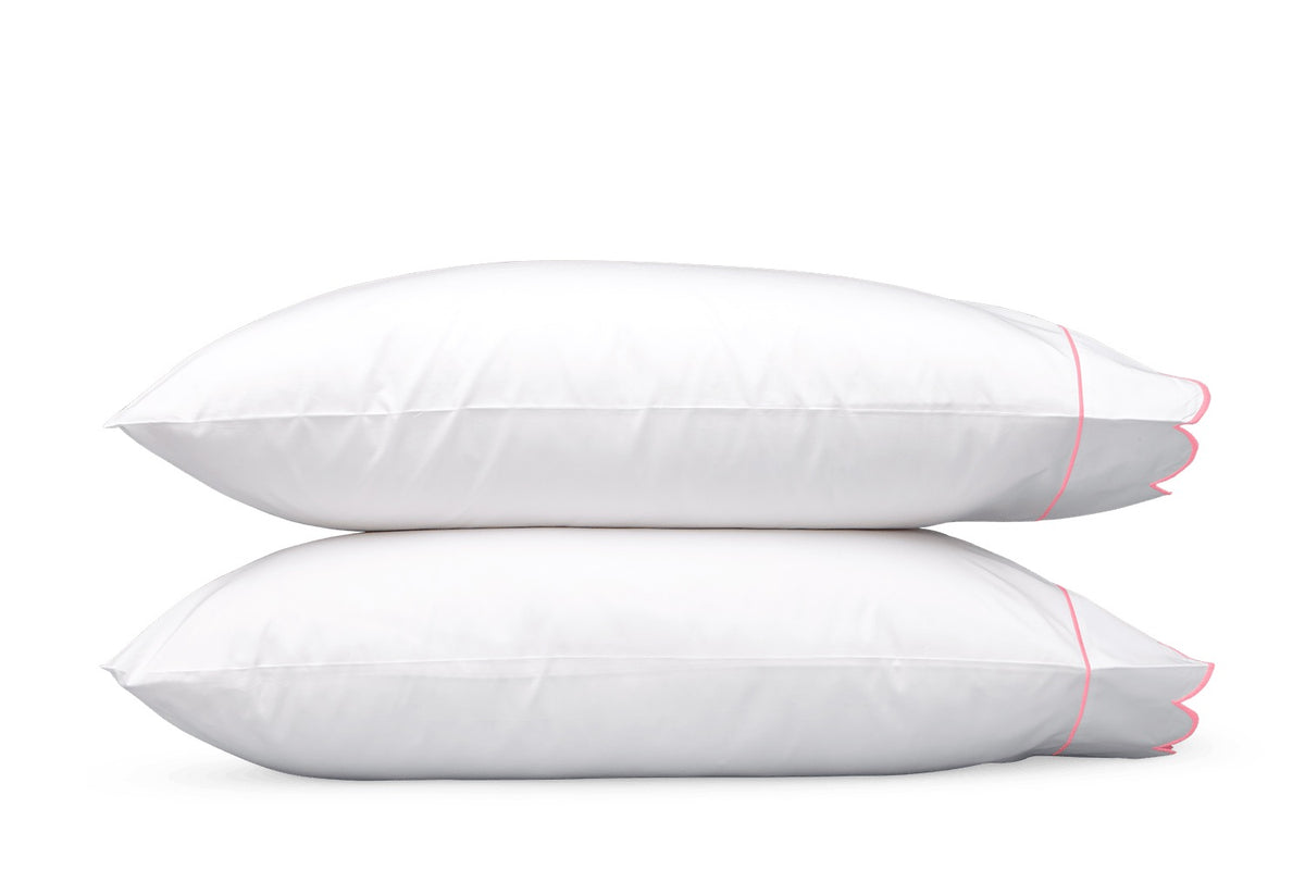 Two white pillows from the Matouk Butterfield Bedding Collection, featuring pink piping and delicate scallop detailing, are stacked horizontally against a plain white background.