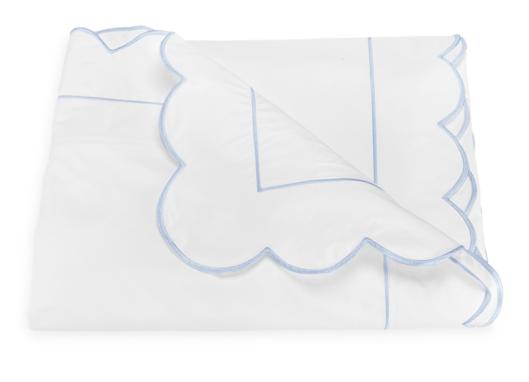 A folded white blanket from the Matouk Butterfield Bedding Collection, Blue, features blue scallop detailing and line accents, crafted from soft Egyptian cotton percale, displayed on a plain background.