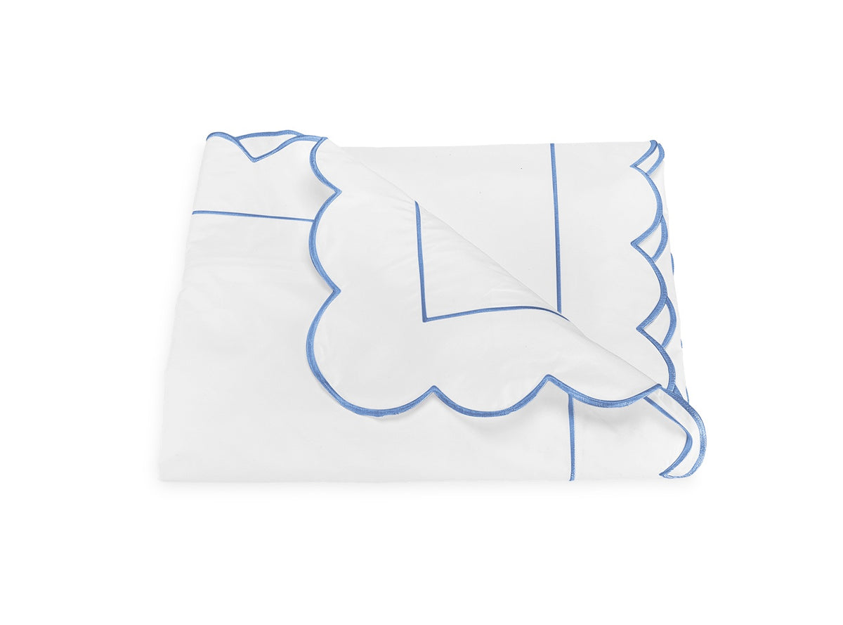 Folded white blanket from the Butterfield Bedding Collection by Matouk, featuring blue scalloped trim and linear blue detailing, crafted from luxurious Egyptian cotton sheets and displayed on a plain white background.