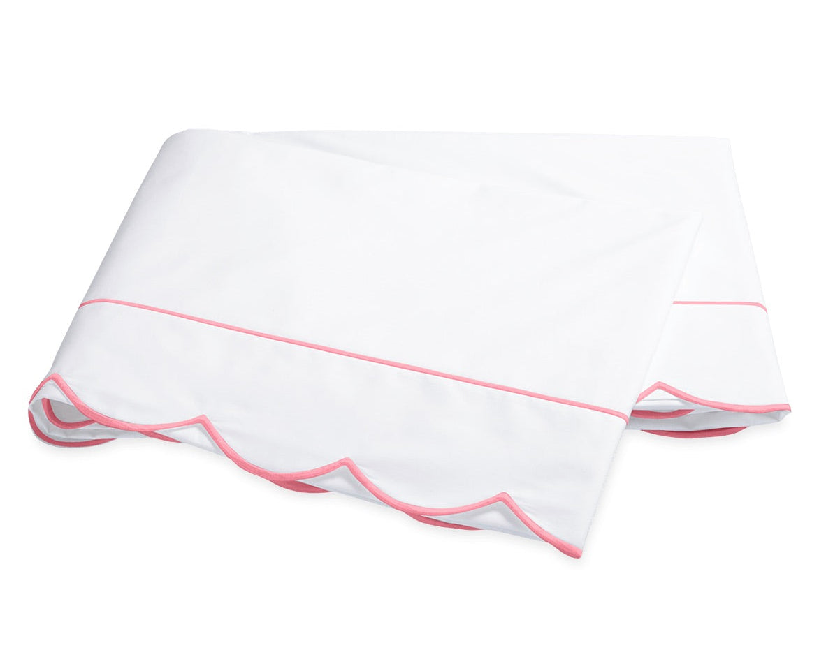 The Butterfield Bedding Collection by Matouk showcases a white folded bedsheet crafted from luxurious percale sheeting, accented with a pink scallop detail and a delicate pink line near the edge, displayed on a plain background.