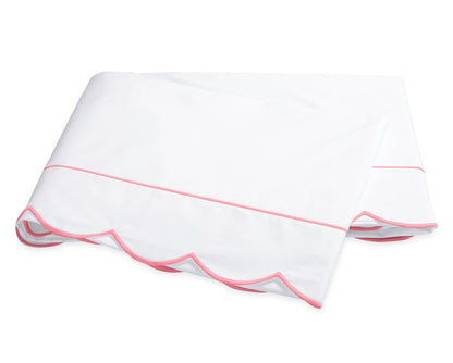 The Butterfield Bedding Collection by Matouk showcases a white folded bedsheet crafted from luxurious percale sheeting, accented with a pink scallop detail and a delicate pink line near the edge, displayed on a plain background.