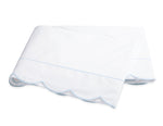 A folded white bedsheet from the Matouk Butterfield Bedding Collection, featuring scallop detailing and light blue trim, crafted from smooth percale sheeting and shown on a plain white background.