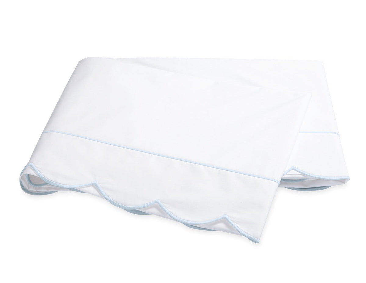 A folded white bedsheet from the Matouk Butterfield Bedding Collection, featuring scallop detailing and light blue trim, crafted from smooth percale sheeting and shown on a plain white background.