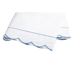 The Butterfield Bedding Collection by Matouk features a white folded bedsheet with elegant scallop detailing and light blue trim, crafted from luxurious Egyptian cotton and displayed on a plain white background.