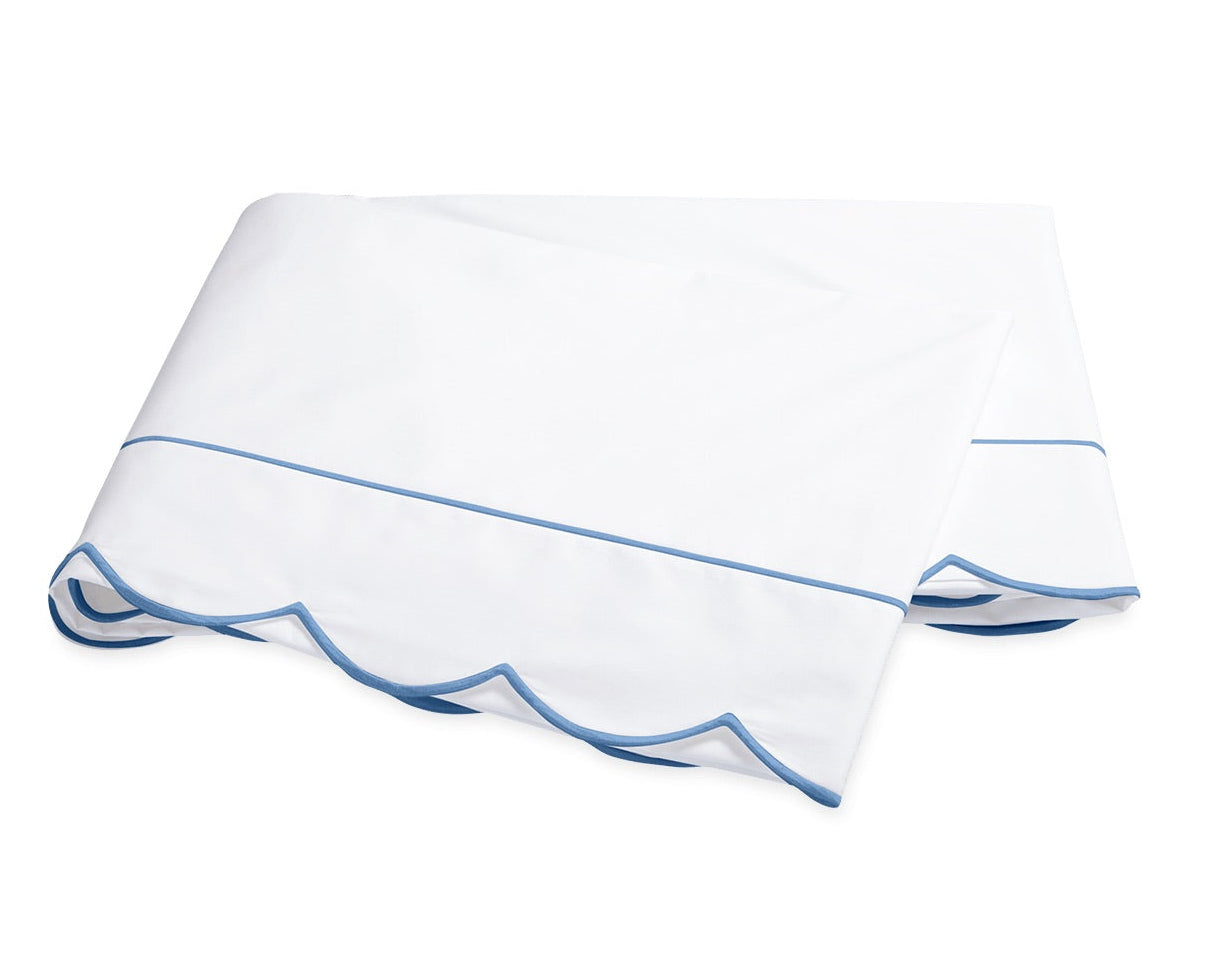 The Butterfield Bedding Collection by Matouk features a white folded bedsheet with elegant scallop detailing and light blue trim, crafted from luxurious Egyptian cotton and displayed on a plain white background.