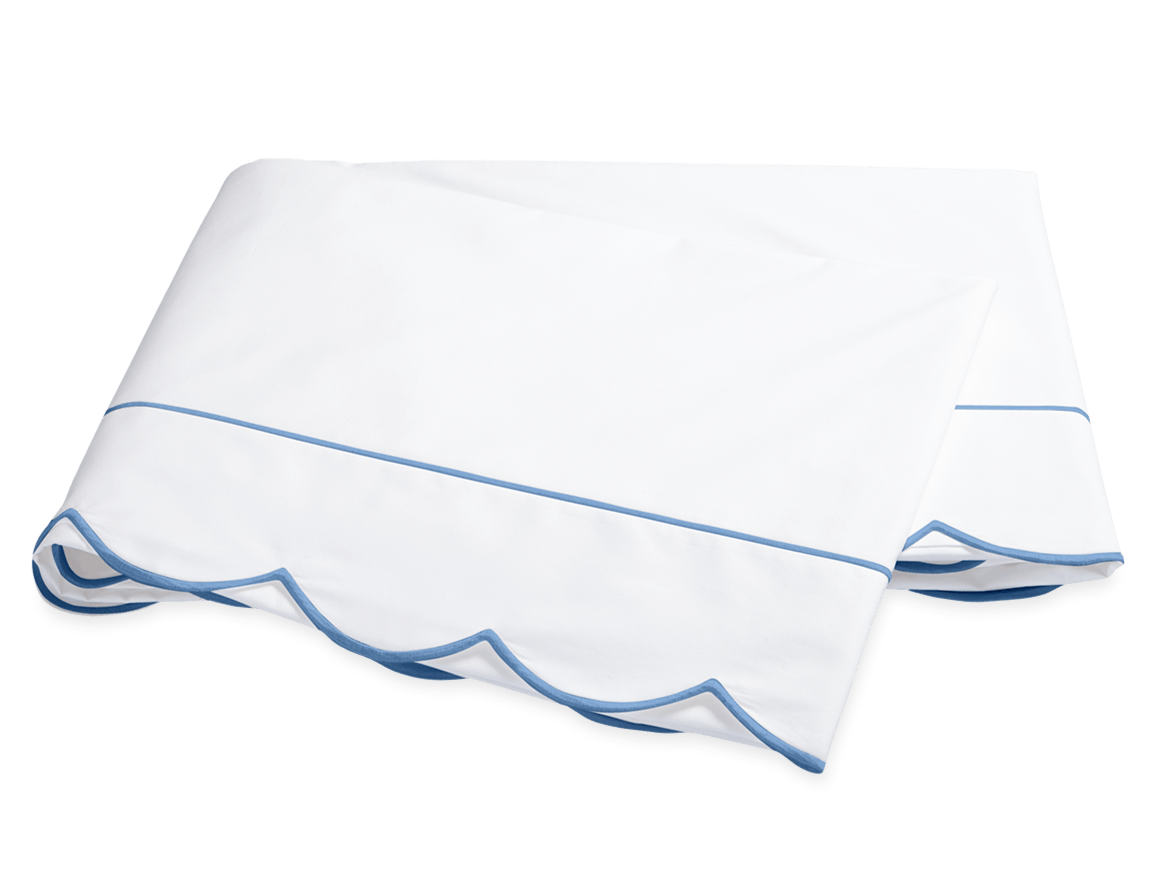 A folded white bedsheet from the Matouk Butterfield Bedding Collection, Ocean, featuring blue scallop detail and a thin blue line, shown on a plain background.
